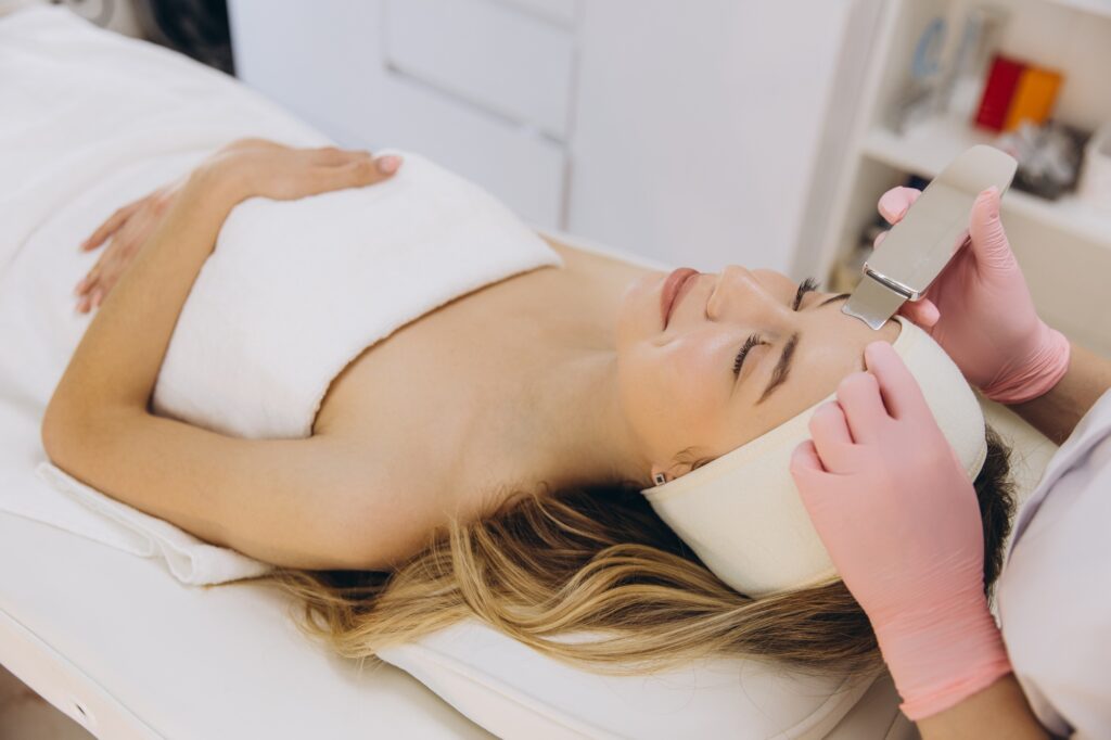 Beautician using ultrasonic scrubber for deep cleansing facial treatment on a relaxed client