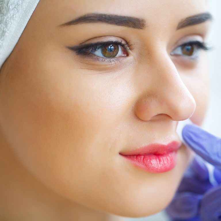 Beautician waxing young woman's eyebrows in spa center